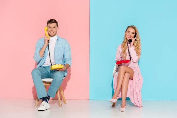 smiling couple sitting and having conversation on vintage telephones with pink and blue background