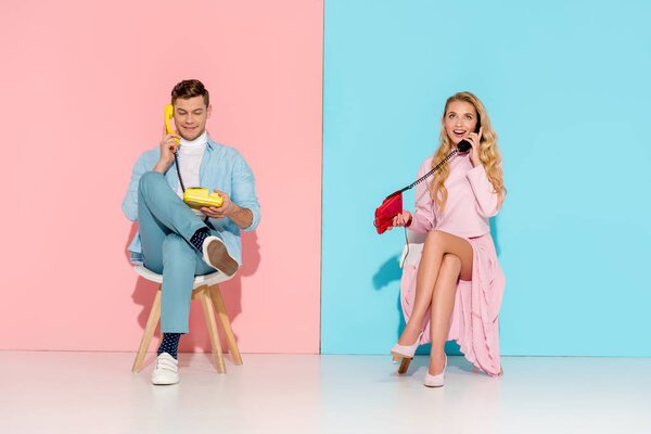 beautiful couple sitting and having conversation on vintage telephones with pink and blue background