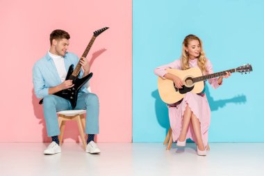 beautiful couple playing electric and acoustic guitars on pink and blue background clipart