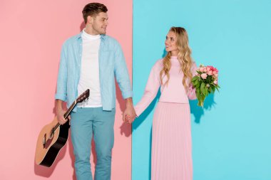Elele ve pembe ve mavi arka plan üzerinde birbirine bakarak akustik gitar ve çiçek buketi çift
