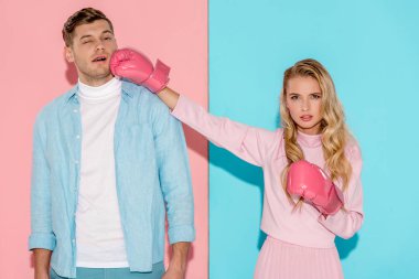 angry woman in boxing gloves hitting man in face on pink and blue background clipart