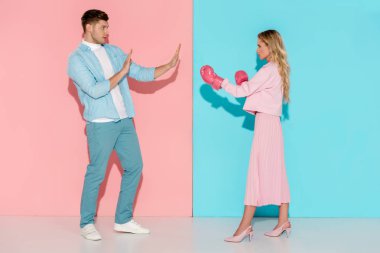 man gesturing with hands near aggressive woman in pink boxing gloves on pink and blue background clipart