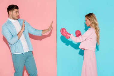 frightened man gesturing with hands near aggressive woman in pink boxing gloves on pink and blue background clipart