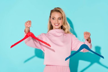 beautiful smiling woman holding empty clothes hangers on turquoise background