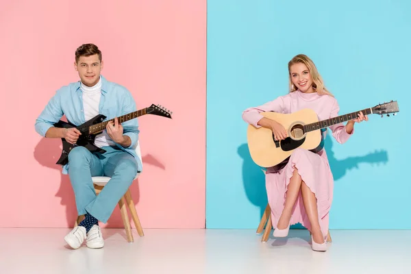 情侣们坐在椅子上 一边弹着电吉他和音响吉他 一边看着粉红色和蓝色背景的相机 — 图库照片