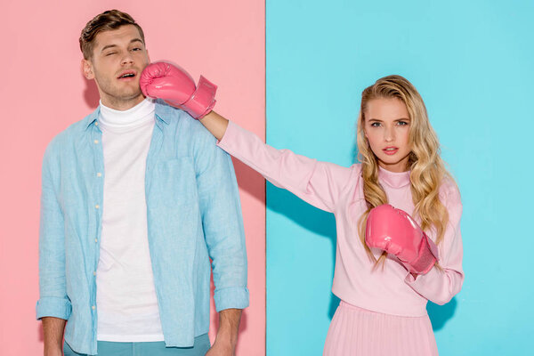 angry woman in boxing gloves hitting man in face on pink and blue background
