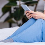 Cropped image of woman resting in bed and using smartphone at home on weekend