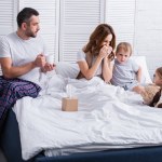 Children supporting sick mother in bedroom, husband holding cup of tea