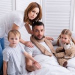 Femme et enfants prenant soin de père malade dans la chambre, regardant la caméra