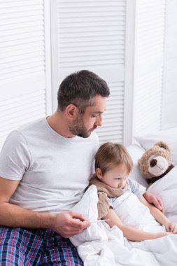 Yatak odasında hasta oğlu bakımı ve vücut ısısı termometresi ile denetleniyor yakışıklı babası