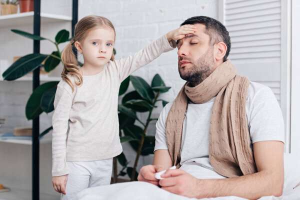 adorable daughter touching sick father forehead and checking temperature in bedroom