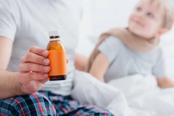 Imagen Recortada Padre Cuidando Hijo Enfermo Dormitorio Mostrando Botella Medicamentos —  Fotos de Stock