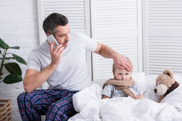 Father Talking Smartphone Touching Sick Son Forehead Bedroom — Stock Photo, Image