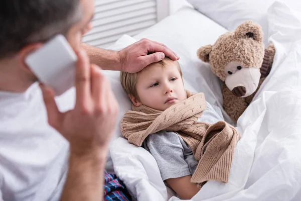 Babanın Smartphone Ile Konuşmak Yatak Odasında Hasta Oğlu Alnına Dokunmak — Stok fotoğraf