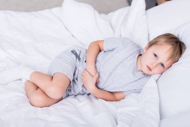 kameraya bakarak yatakta yatarken ve yatak, acı mide dokunmadan hasta çocuk