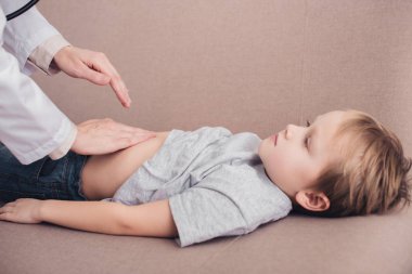 hasta çocuk mide oturma odasında kanepede palpating pediatrist görüntü kırpılmış