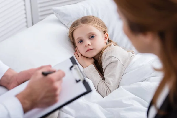 Selective Focus Pediatrist Writing Something Clipboard Sick Kid Looking Camera — Stock Photo, Image