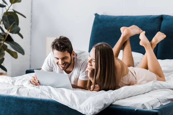 Jovem Casal Sorrindo Deitado Cama Com Pernas Cruzadas Usando Laptop — Fotografia de Stock