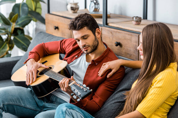 young girl sitting on sofa with boyfriend while listening to guitar music
