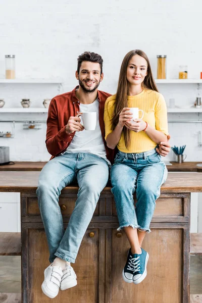 Cheerful Couple Sitting Wooden Table Kitchen Holding Cups — Free Stock Photo
