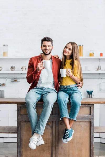 Glückliches Paar Sitzt Auf Holztisch Küche Und Hält Tassen — Stockfoto