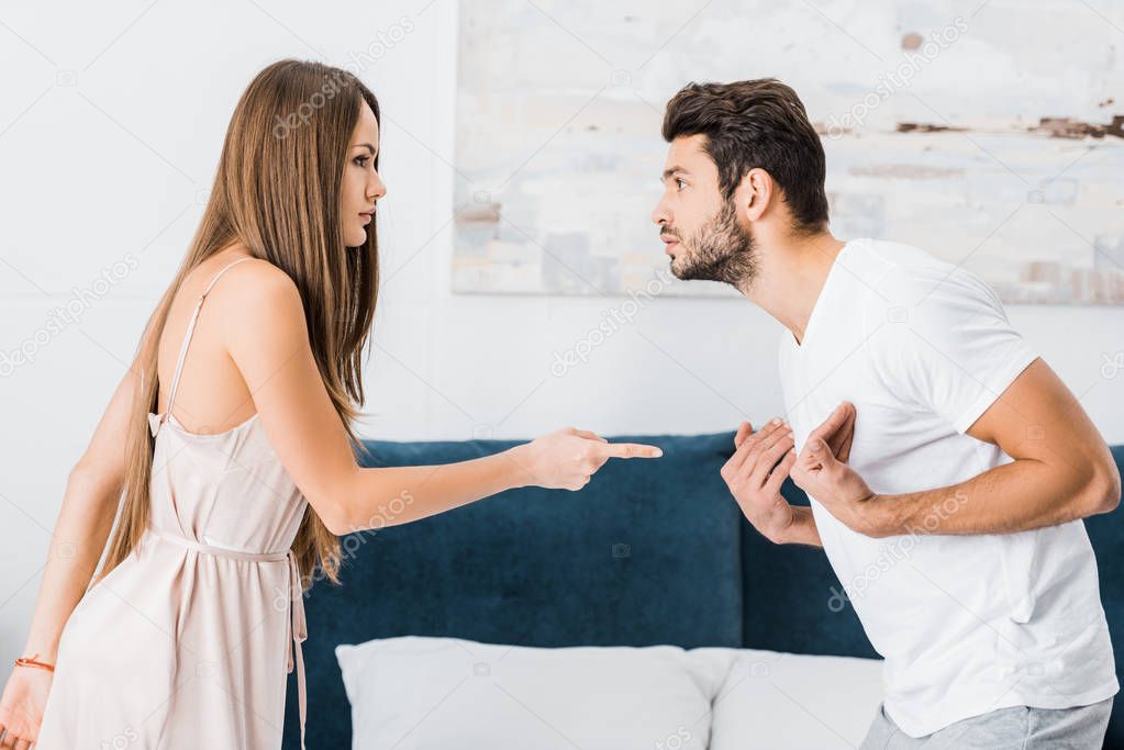 young attractive woman pointing with finger angrily at stressed gesturing man