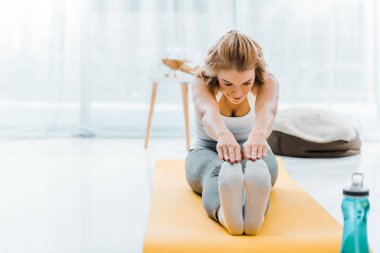 Kadın sarı fitness mat oturma odasında germe egzersiz yaparak spor giyim