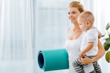 spor giyim holding mavi fitness mat ve yürümeye başlayan çocuk boy gülümseyerek güzel kadın