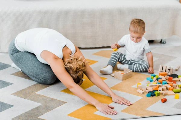 Kvinnan Gör Stretching Övning Mattan Och Småbarn Pojke Leker Med — Gratis stockfoto