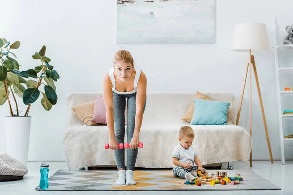 Attractive Woman Doing Exercise Dumbbells Looking Camera Cute Toddler Boy — Free Stock Photo