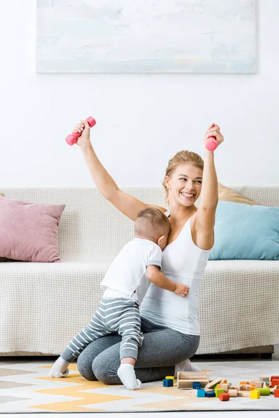 Smiling Woman Holding Dumbbells Raising Hands Toddler Boy Embracing Mother — Stock Photo, Image