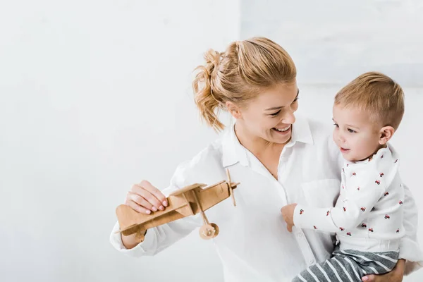 Woman Smiling Holding Wooden Plane Model Playing Cute Toddler Boy — Stock Photo, Image
