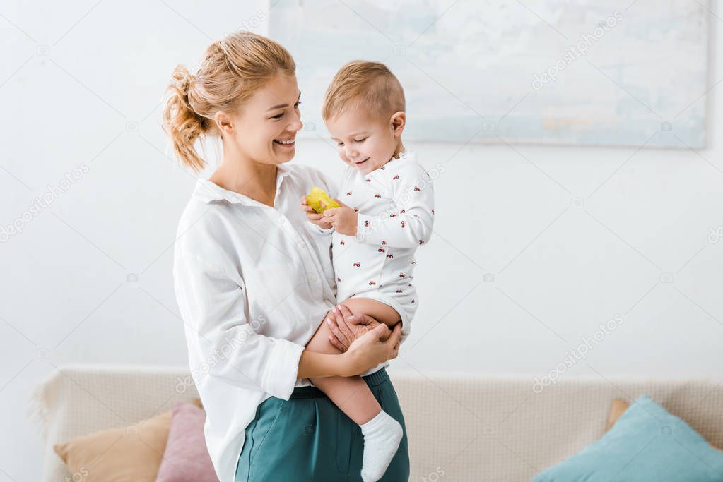smiling woman standing and holding toddler son in living room