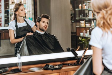 female hairstylist cutting hair to handsome young man in beauty salon clipart