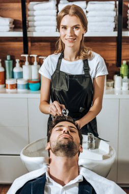 Güzellik salonunda yakışıklı adama saç yıkarken kameraya gülümseyen güzel Kuaför