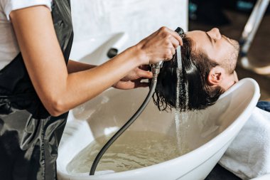 Güzellik salonunda yakışıklı genç erkek istemciye saç yıkama Kuaför kısmi görünümünü 