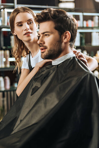 young female hairstylist looking at handsome man in beauty salon 