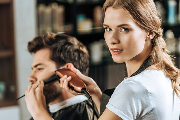 Ελκυστική Hairstylist Βλέπουν Φωτογραφική Μηχανή Ενώ Ψαλίδισμα Των Τριχών Άνδρες — Φωτογραφία Αρχείου