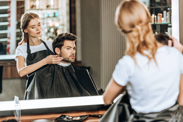 reflection in mirror of hairdresser doing hairstyle to handsome client in beauty salon