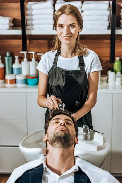 Hermosa Peluquera Sonriendo Cámara Mientras Lava Cabello Hombre Guapo Salón — Foto de Stock