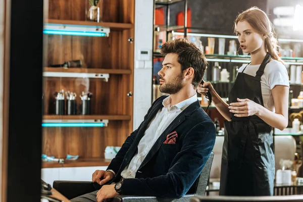 Jovem Cabeleireiro Feminino Segurando Secador Cabelo Olhando Para Bonito Cliente — Fotografia de Stock