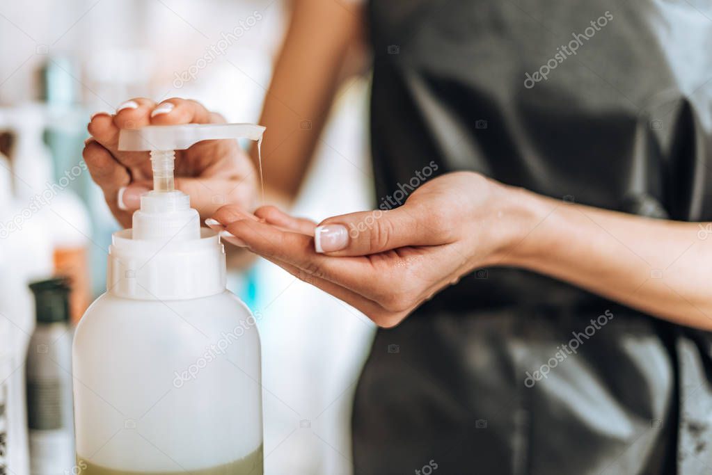 close-up partial view of young hairstylist holding lotion in beauty salon