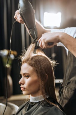 cropped shot of hairstylist drying hair to beautiful young woman in beauty salon  clipart