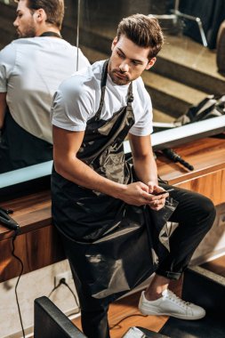 smartphone kullanarak ve uzak güzellik salonunda seyir yakışıklı genç Kuaför yüksek açılı görünüş