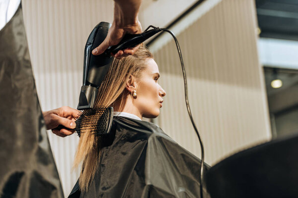 low angle view of hairdresser drying hair to attractive girl in beauty salon  