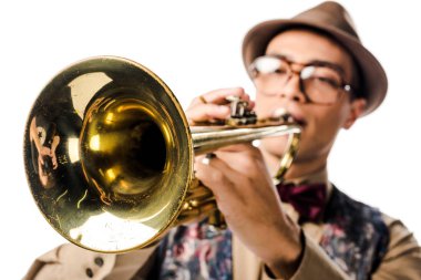 selective focus of mixed race male musician in stylish hat and eyeglasses playing on trumpet isolated on white  clipart