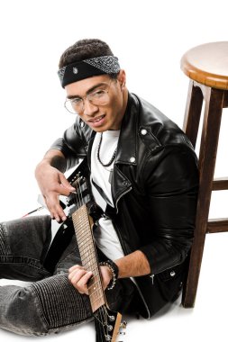 neşeli genç erkek rock müzisyeni sandalye üzerinde beyaz izole yakın katta otururken elektrik gitar çalmaya deri ceketli