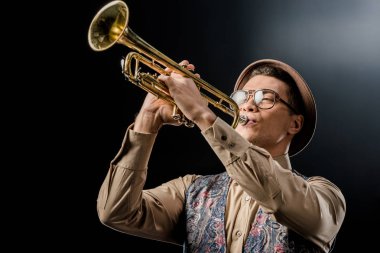 Genç erkek jazzman şapka ve gözlük siyah izole trompet oynamaya