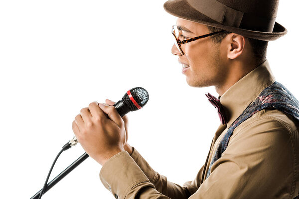 side view of happy mixed race young man in hat singing in microphone isolated on white