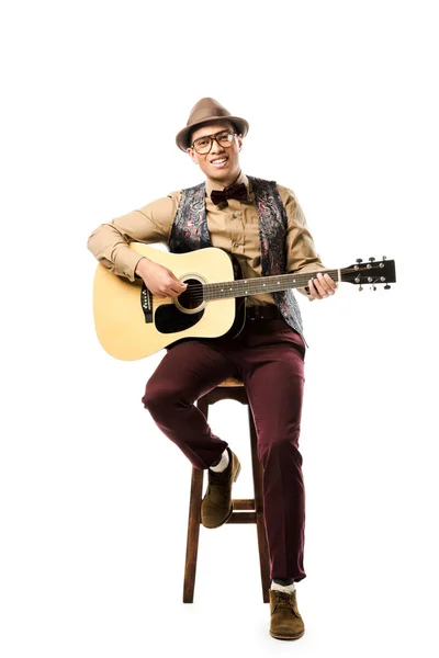 帽子と眼鏡の椅子に座っては 白で隔離中 アコースティック ギターの演奏で陽気な混血男性ミュージシャン — ストック写真